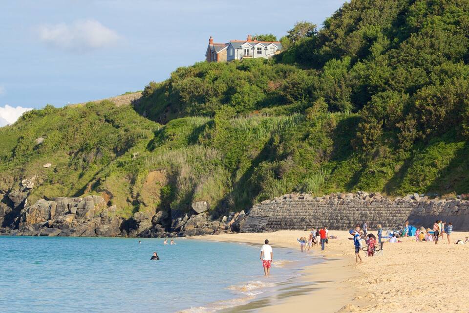 A beach with people, a rocky shoreline, and a house on a hill.