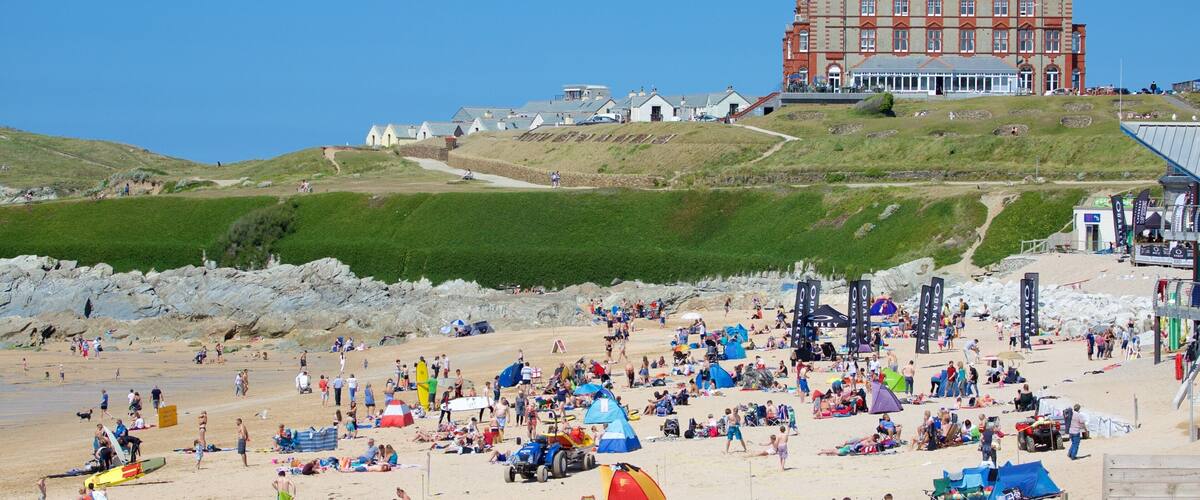 A crowded beach with tents and umbrellas, a large building in the background, and rocky terrain.