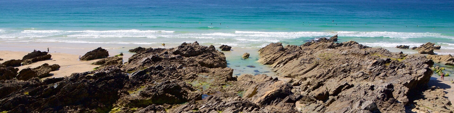 Litoral rochoso com águas turquesa cristalinas e uma praia arenosa.
