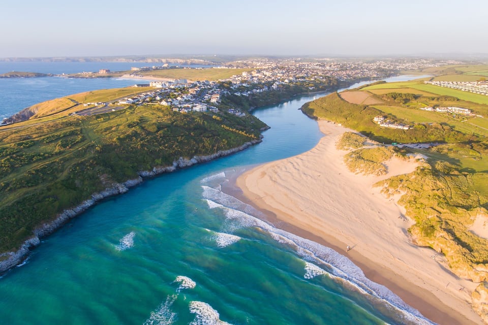 Uma vila costeira com rio, praia e vegetação ao redor.