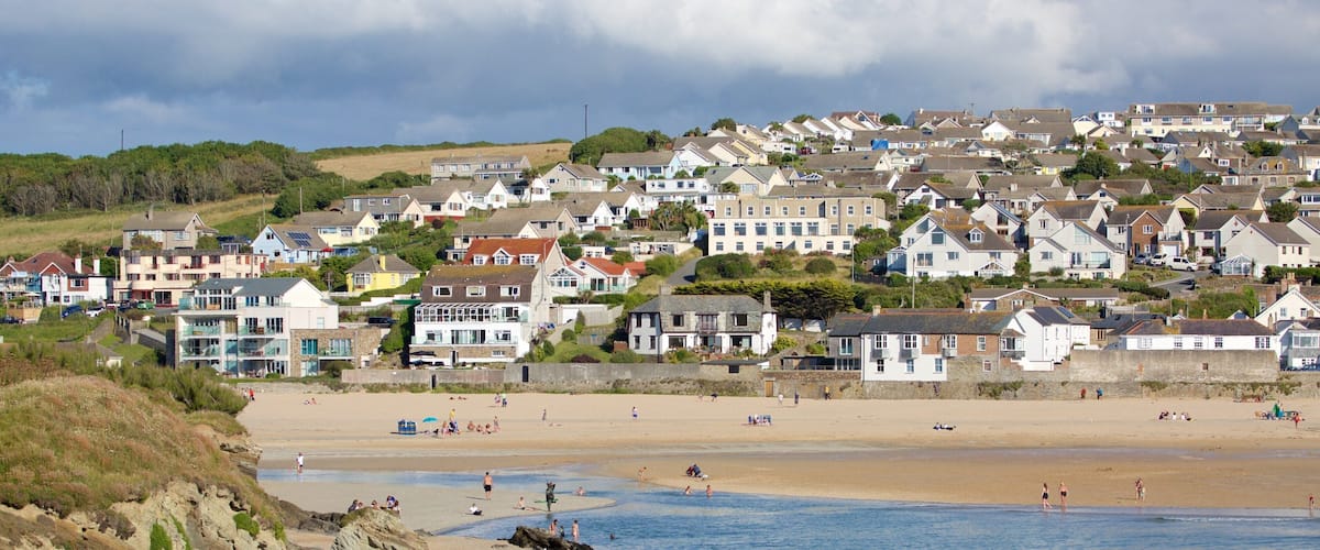 A coastal town with a sandy beach, rocky shoreline, and residential buildings.