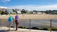 A beach with a metal railing, a sandy shore, and houses in the background.