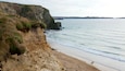 A coastal landscape with cliffs, a sandy beach, and a calm sea.