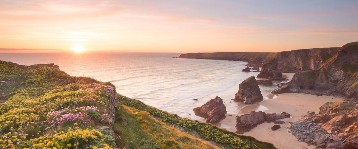 A coastal landscape with cliffs, a sandy beach, and a sunset over the ocean.