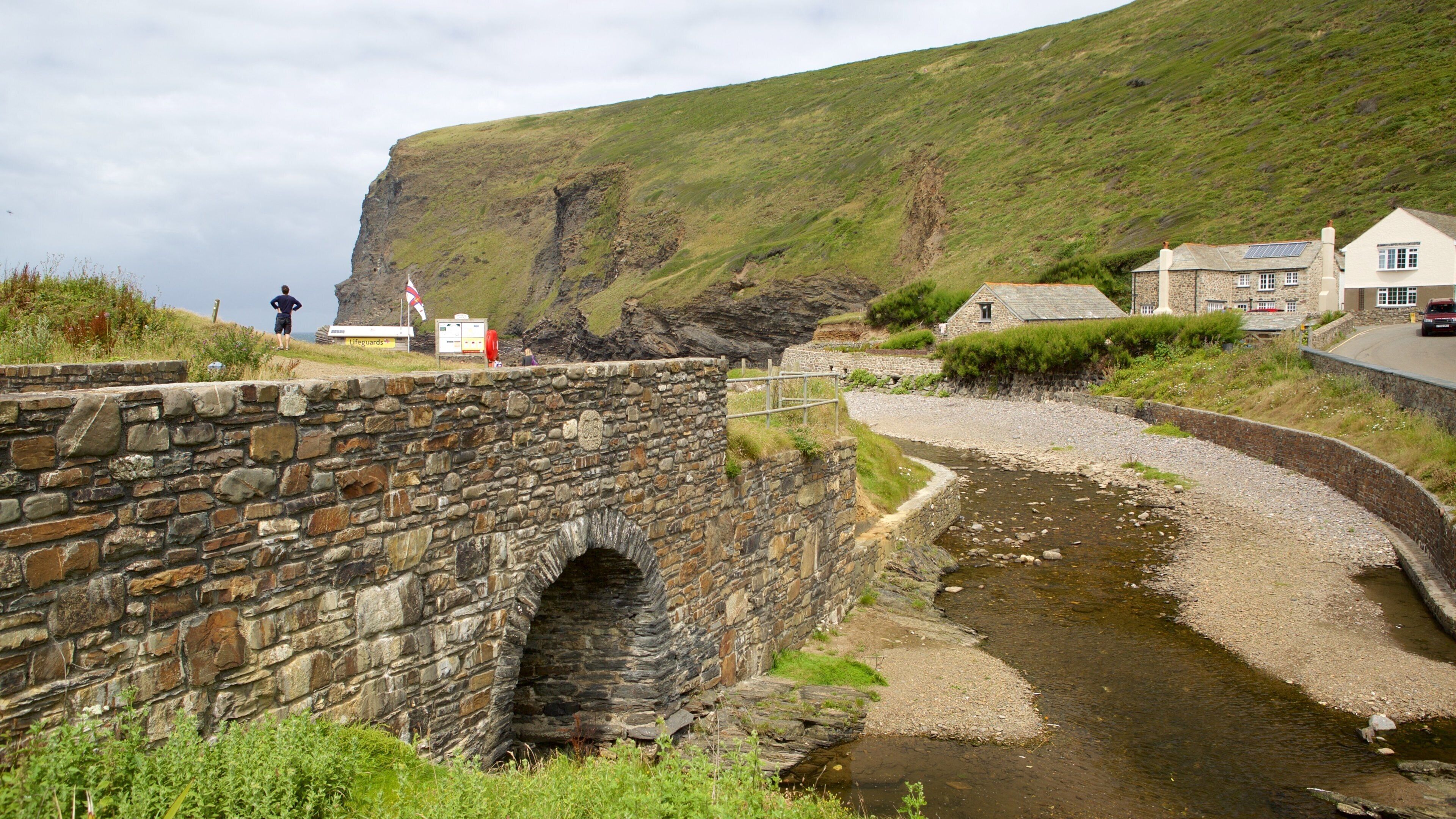 A stone bridge over a stream, a coastal cliff, and houses near the water.