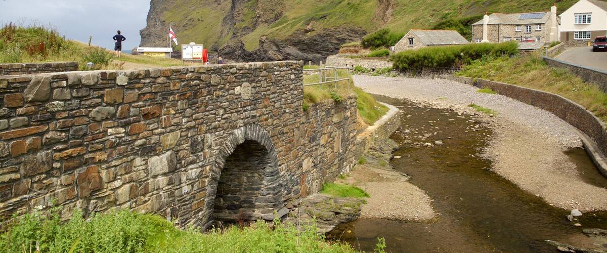 A stone bridge over a stream, a coastal cliff, and houses near the water.