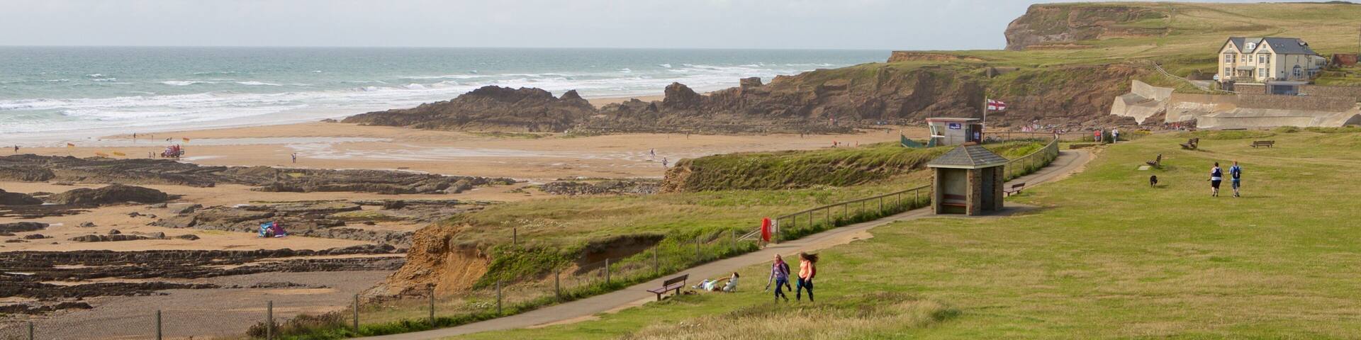 A coastal landscape with a beach, rocky cliffs, a grassy field, and a small building.