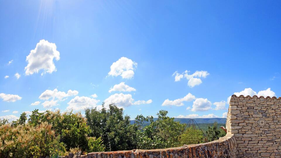 A stone wall, a windmill, and a clear blue sky with clouds.