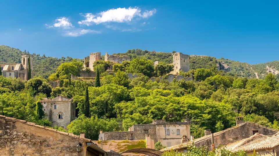 A historic town with medieval ruins on a hillside, surrounded by lush greenery.