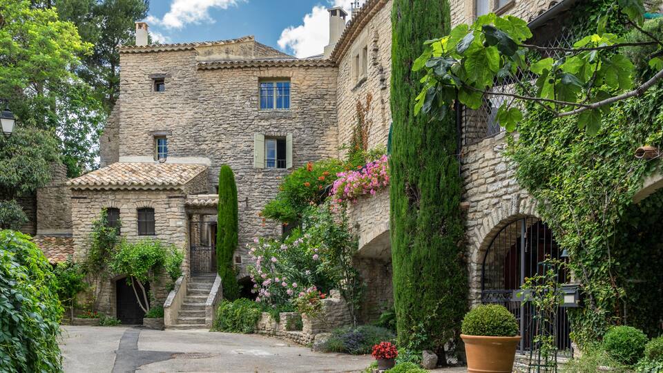 A stone building with a tiled roof, a staircase, and a garden with various plants and flowers.