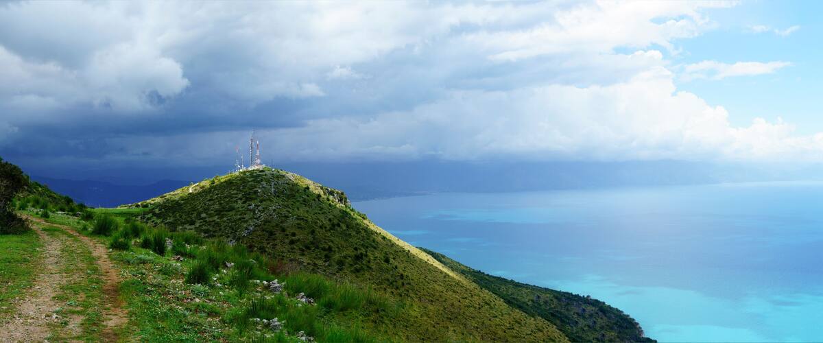 A coastal landscape with a grassy hill, a clear sky, and a distant tower.