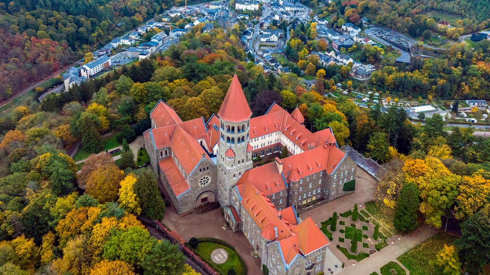 An aerial view of a historic castle surrounded by autumn-colored trees and a small town.