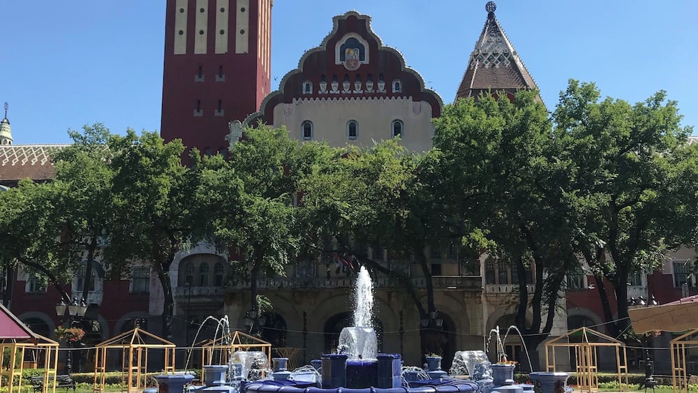 A historic building with a clock tower, a fountain, and a red tower.
