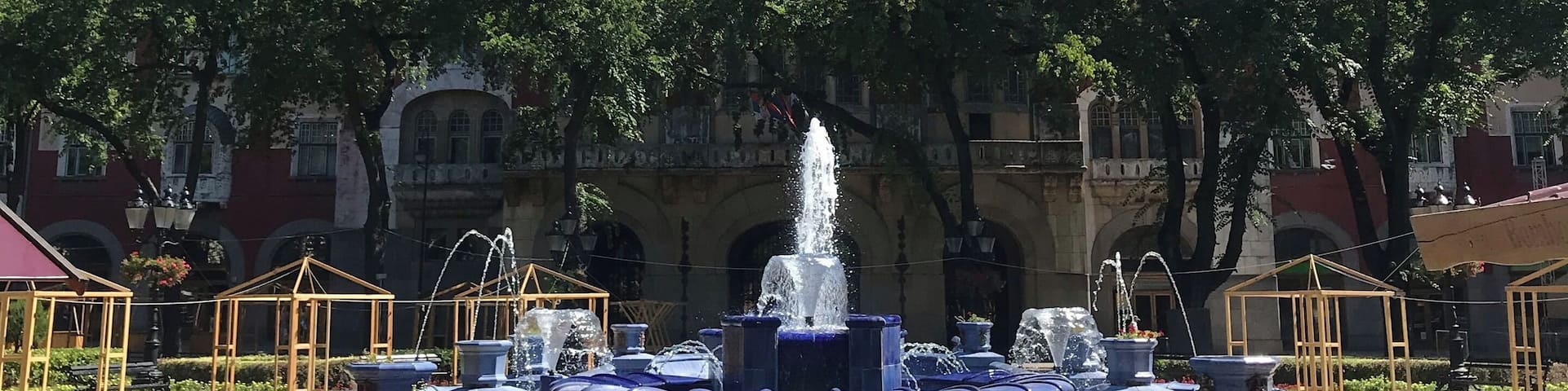 A historic building with a clock tower, a fountain, and a red tower.