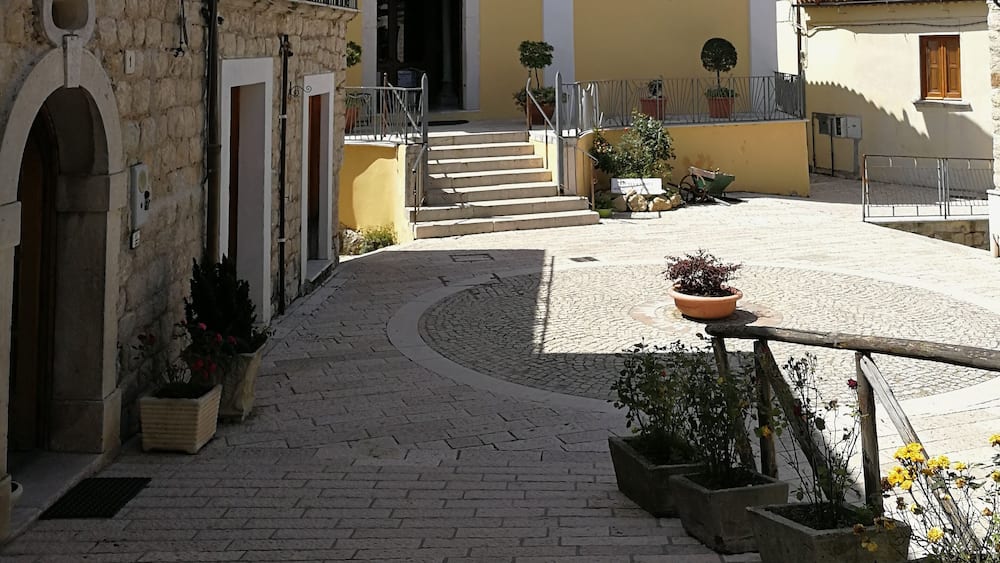 A cobblestone street with a yellow building, stone walls, and potted plants.