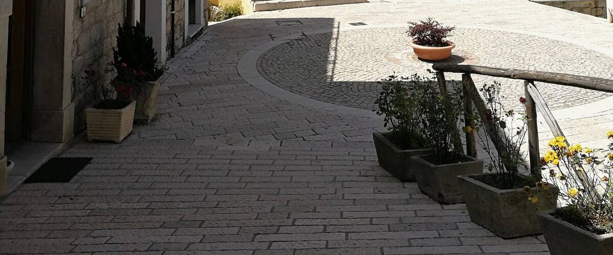 A cobblestone street with a yellow building, stone walls, and potted plants.