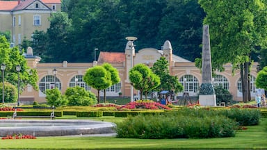 A well-manicured garden with a fountain, trimmed hedges, and a building with arched windows and a dome.