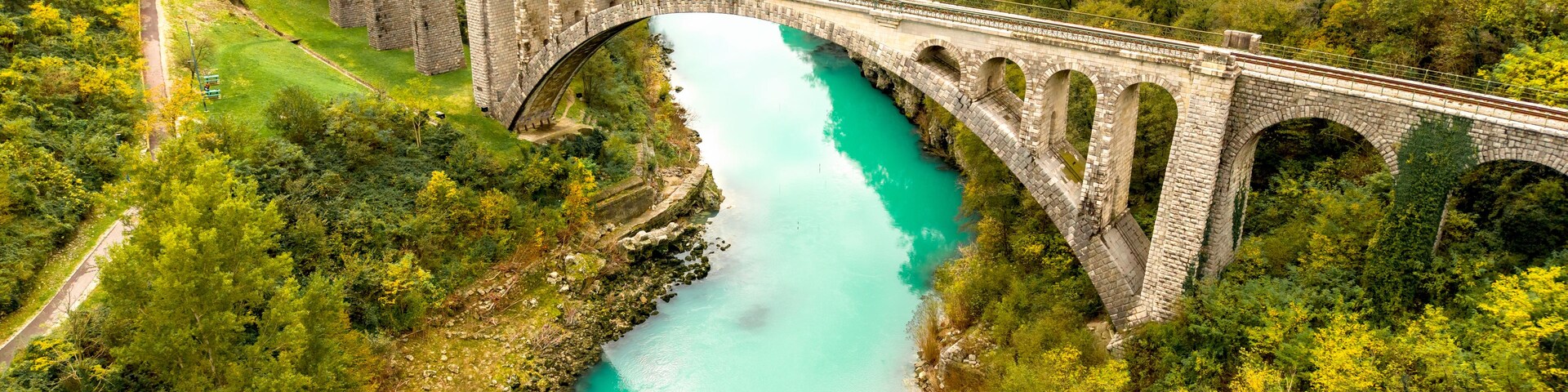 Un puente de piedra sobre un río turquesa, rodeado de abundante vegetación y colinas.