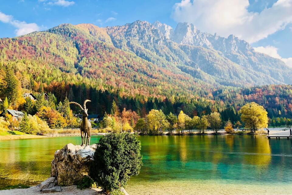 A lake with clear water, surrounded by autumn-colored trees and mountains in the background.