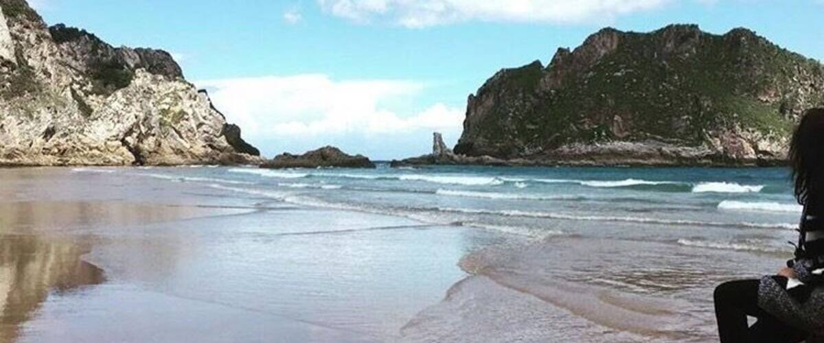 A beach with rocky cliffs, calm waves, and a clear sky.