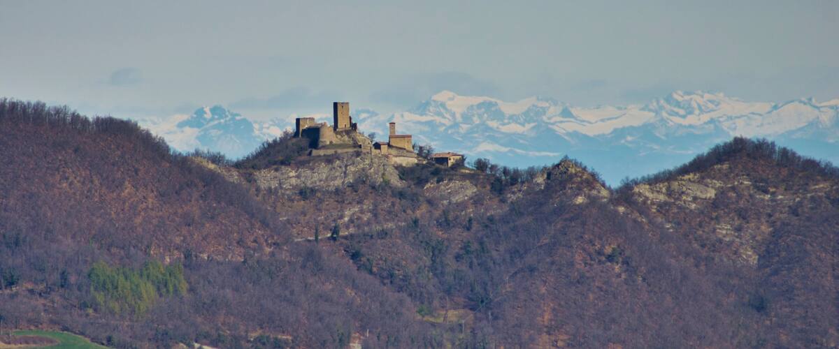 Un castello storico su una collina, con montagne innevate sullo sfondo.