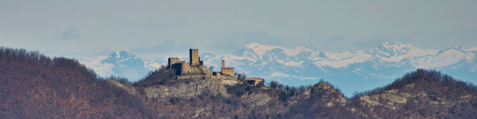 Un castillo histórico sobre una colina, con montañas nevadas al fondo.