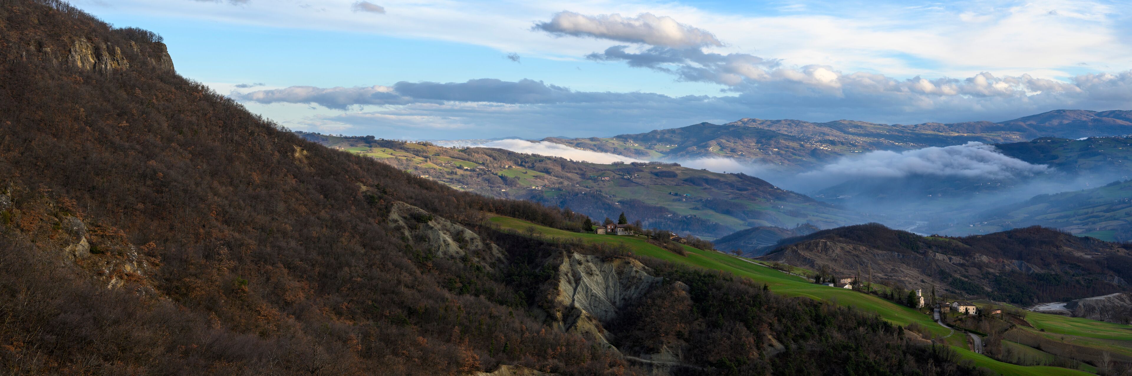 A mountainous landscape with green fields, scattered houses, and a valley with mist.