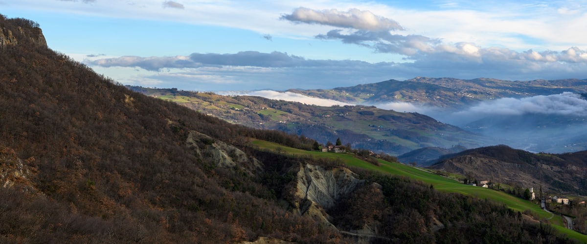 A mountainous landscape with green fields, scattered houses, and a valley with mist.