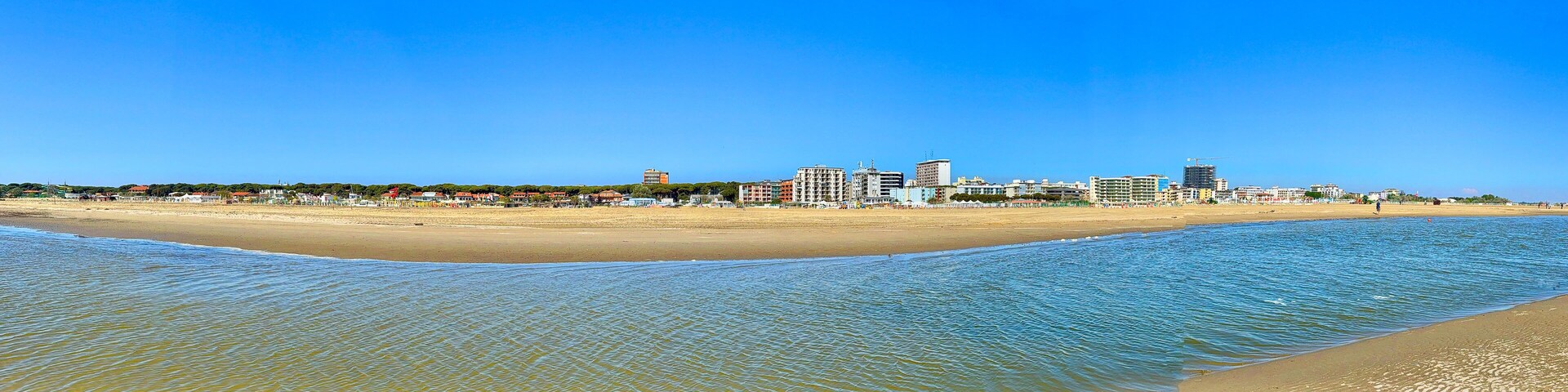 Un paisaje urbano costero con una playa de arena y un mar azul claro.