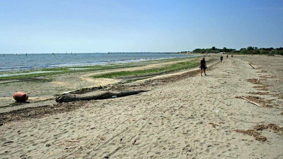 A sandy beach with a few people walking, a large ball, and a pier in the distance.