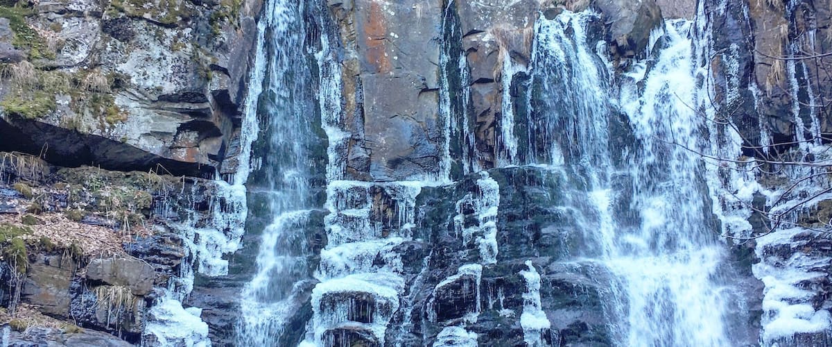 A person standing in front of a multi-tiered waterfall with ice formations.