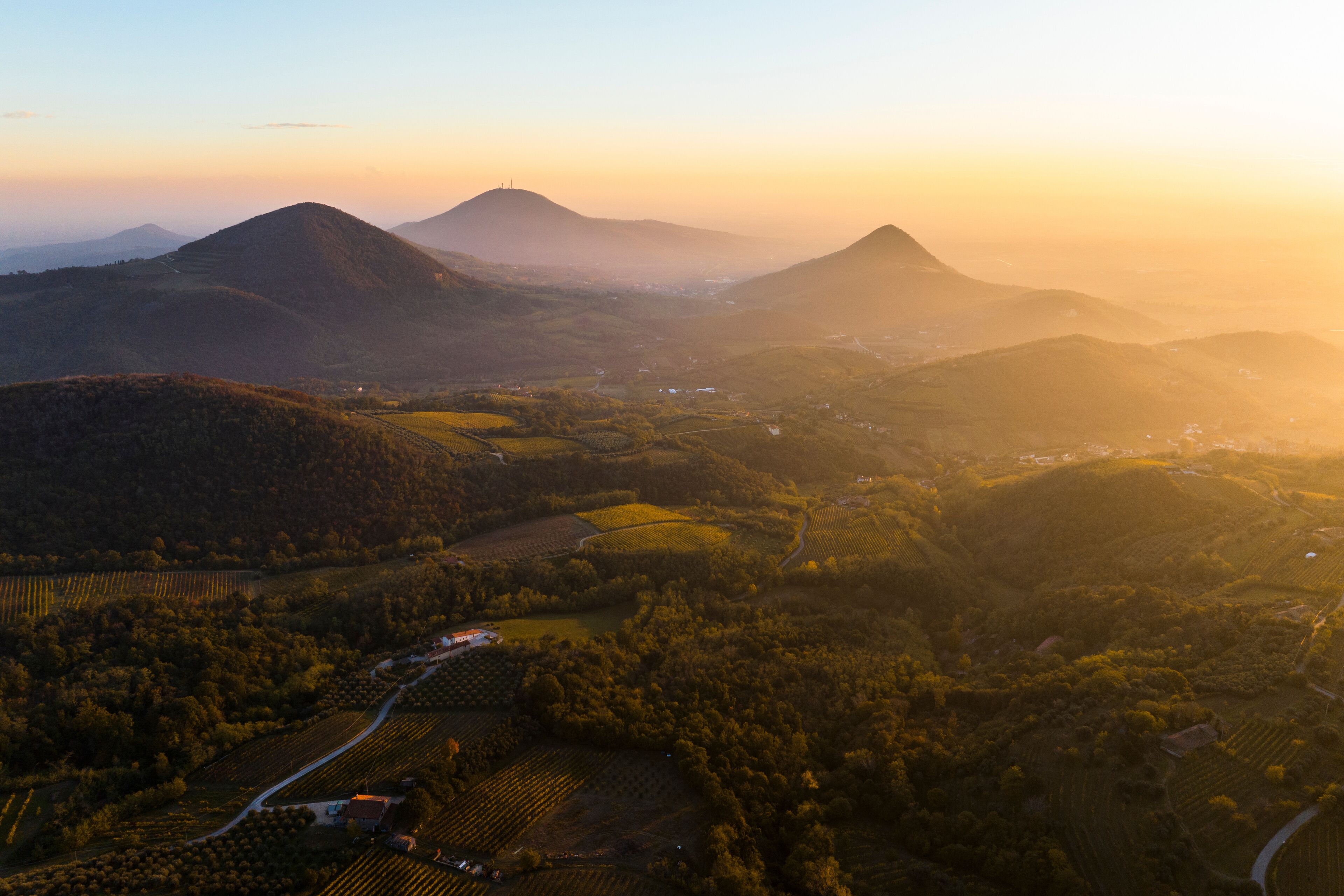 A mountainous landscape with fields and a small settlement during sunrise or sunset.