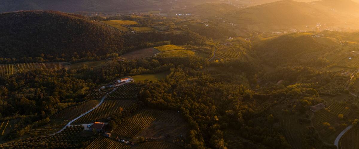 A mountainous landscape with fields and a small settlement during sunrise or sunset.