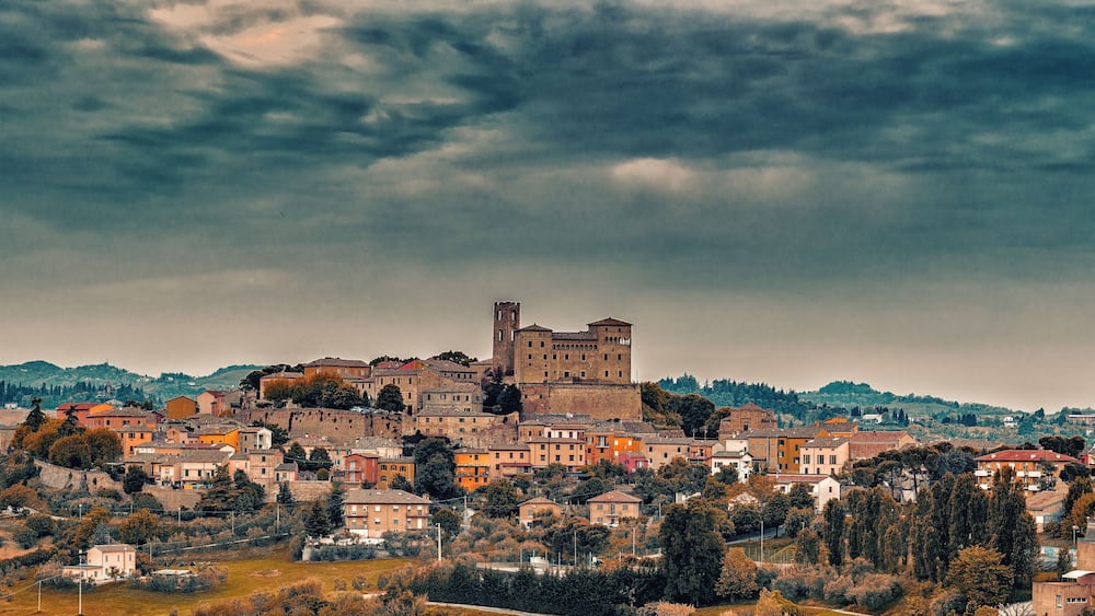 A historic town with a prominent castle on a hill, surrounded by residential buildings and lush greenery.