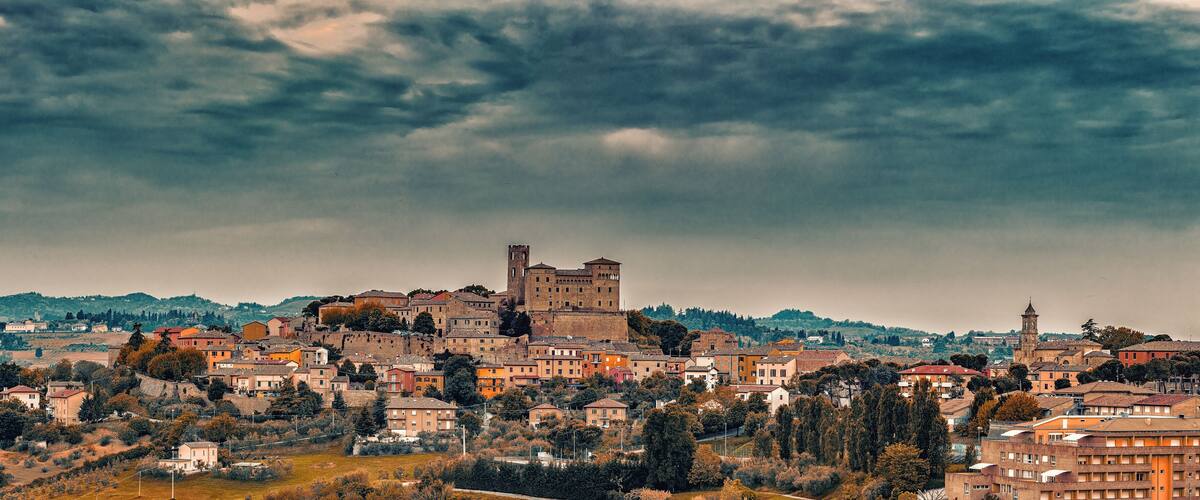 A historic town with a prominent castle on a hill, surrounded by residential buildings and lush greenery.