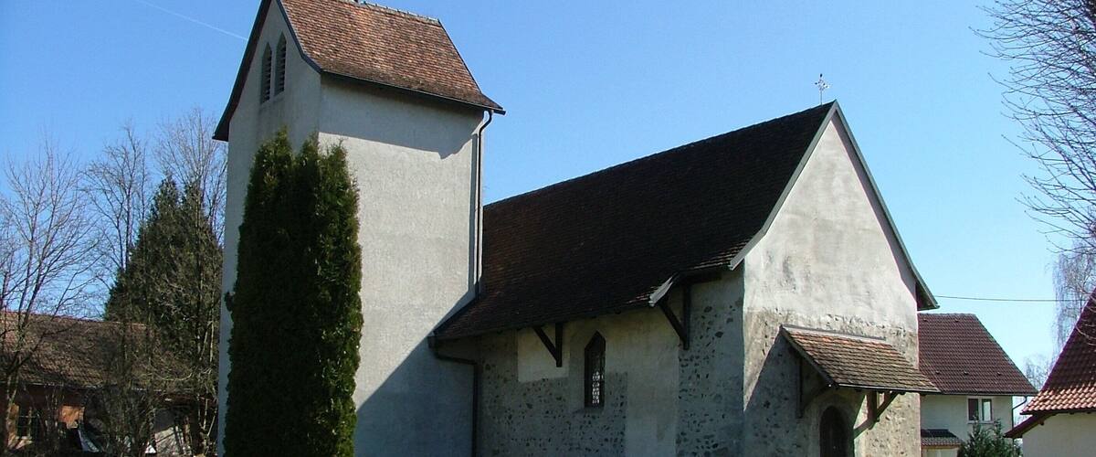 A church with a bell tower and a steeple, surrounded by a grassy area and trees.