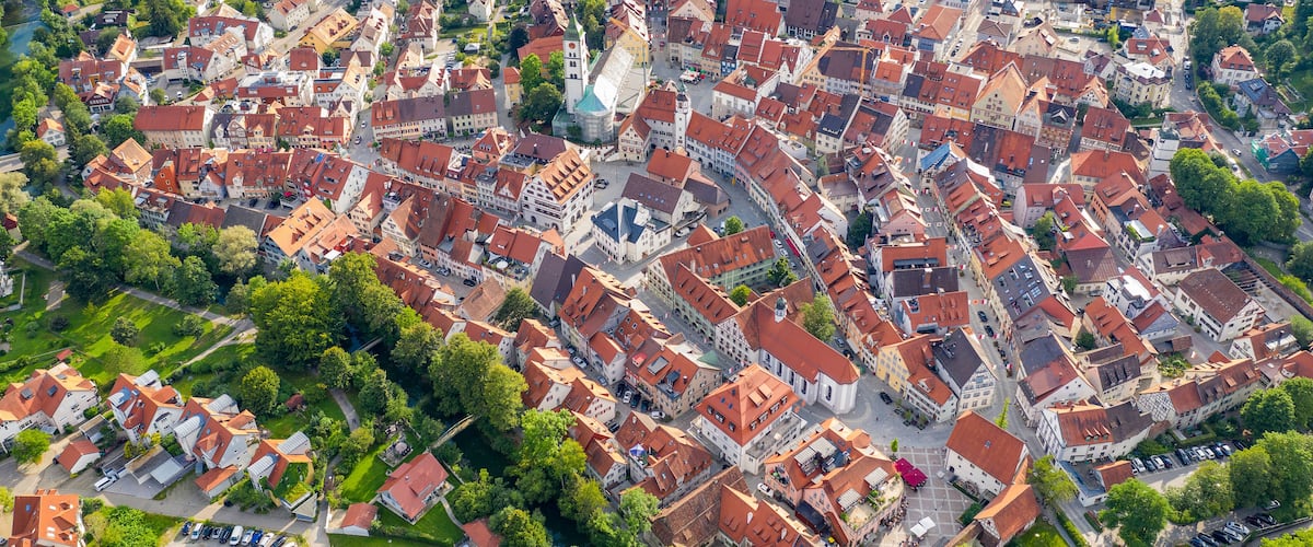 Vista aérea de una localidad densamente poblada con edificios históricos, una imponente torre de iglesia y zonas verdes circundantes.