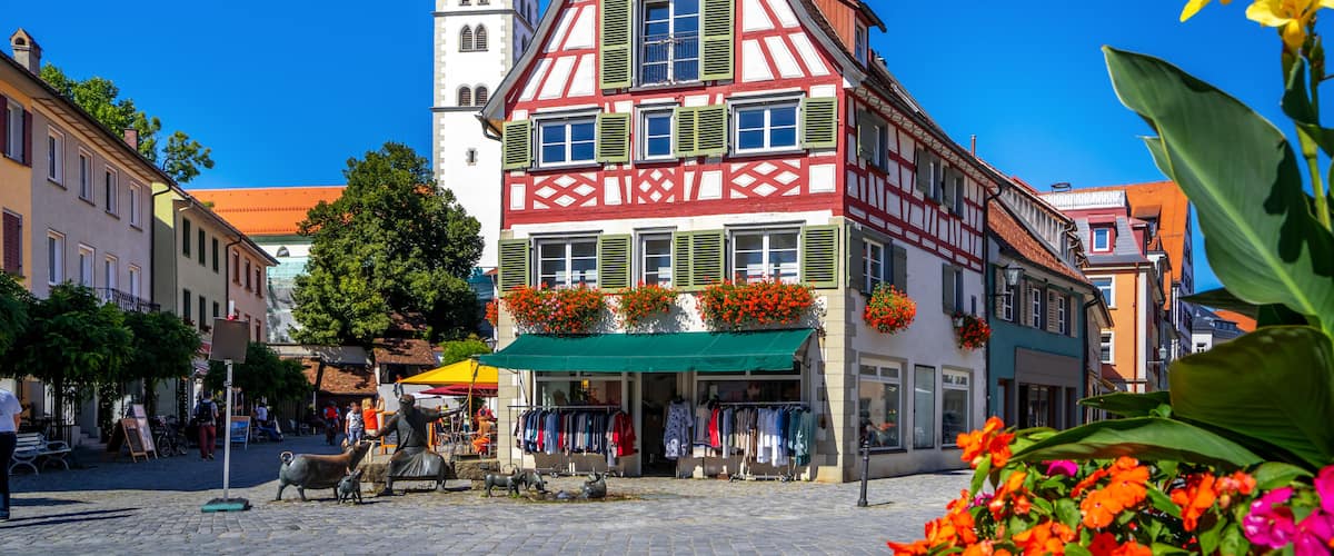 Un edificio tradicional con entramado de madera y una torre de reloj, rodeado de calles empedradas y flores coloridas.