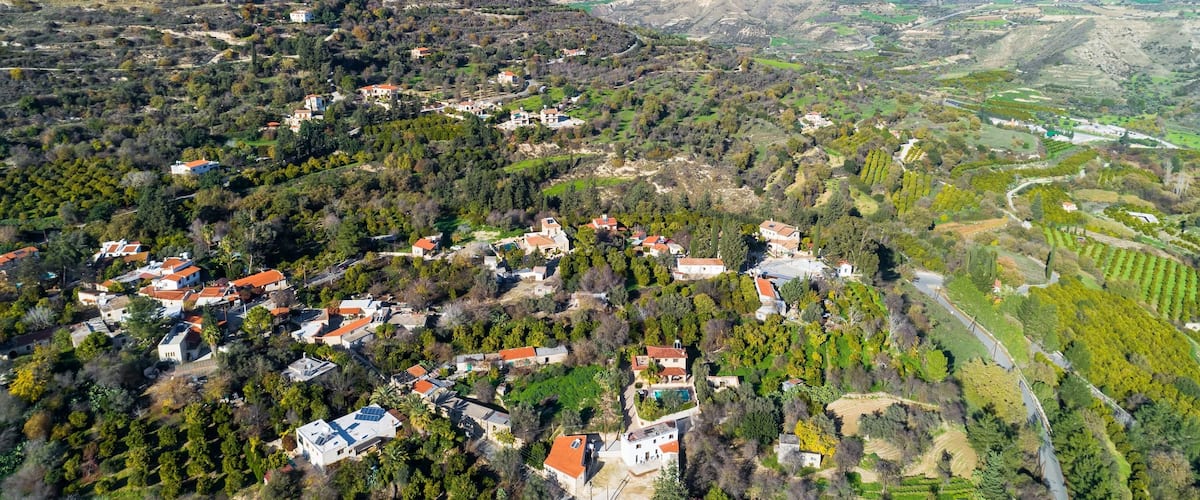 An aerial view of a hilly village with scattered houses, dense greenery, and a river.