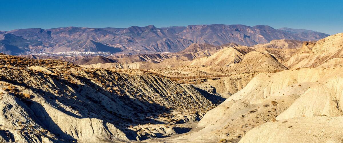 A rugged desert landscape with layered rock formations and distant mountains.