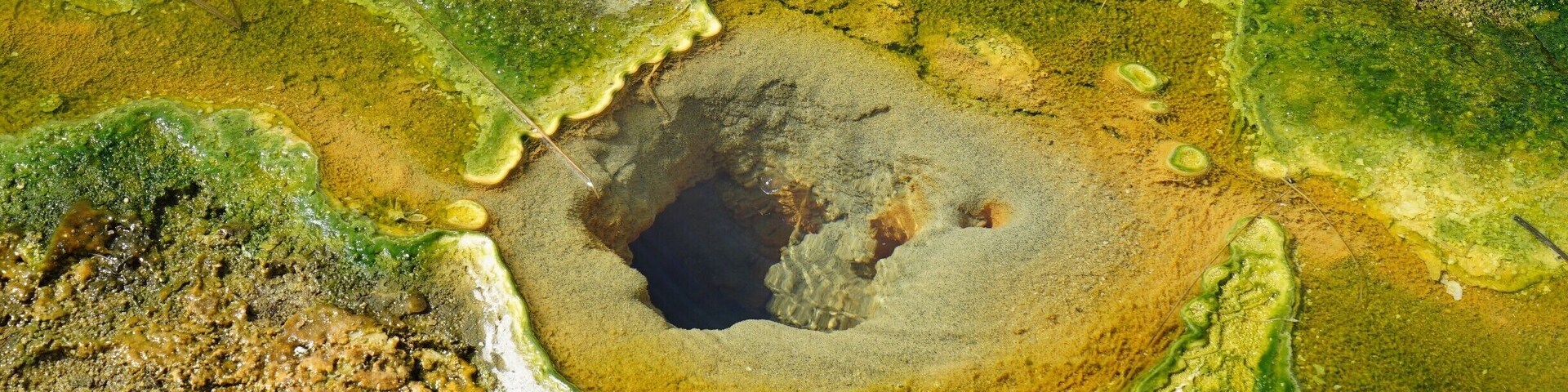 Una fuente termal geotérmica con una depresión central rodeada de depósitos minerales verdes y amarillos.