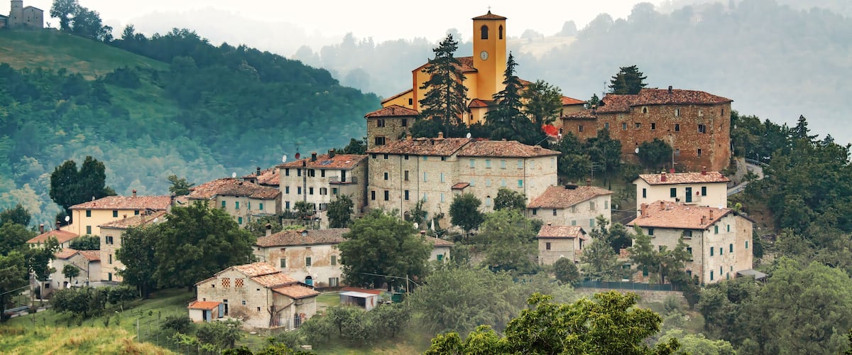 A historic village with a prominent church featuring a bell tower, surrounded by lush greenery and terraced houses.