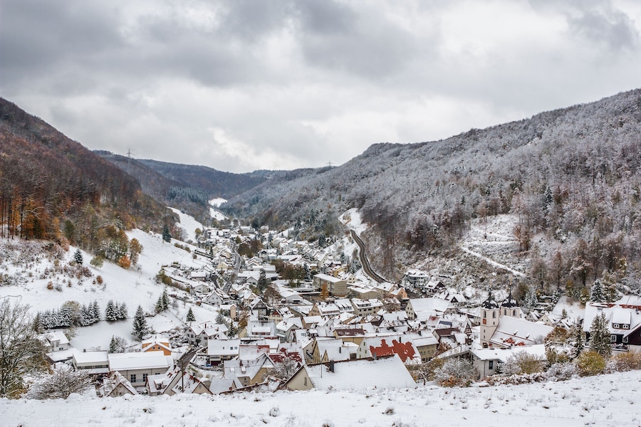 Un pueblo cubierto de nieve situado en un valle, con montañas boscosas al fondo.