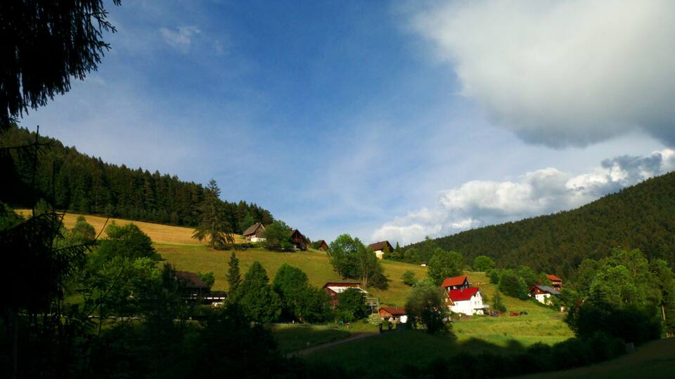 A rural landscape with houses on a hillside, surrounded by trees and a clear sky.