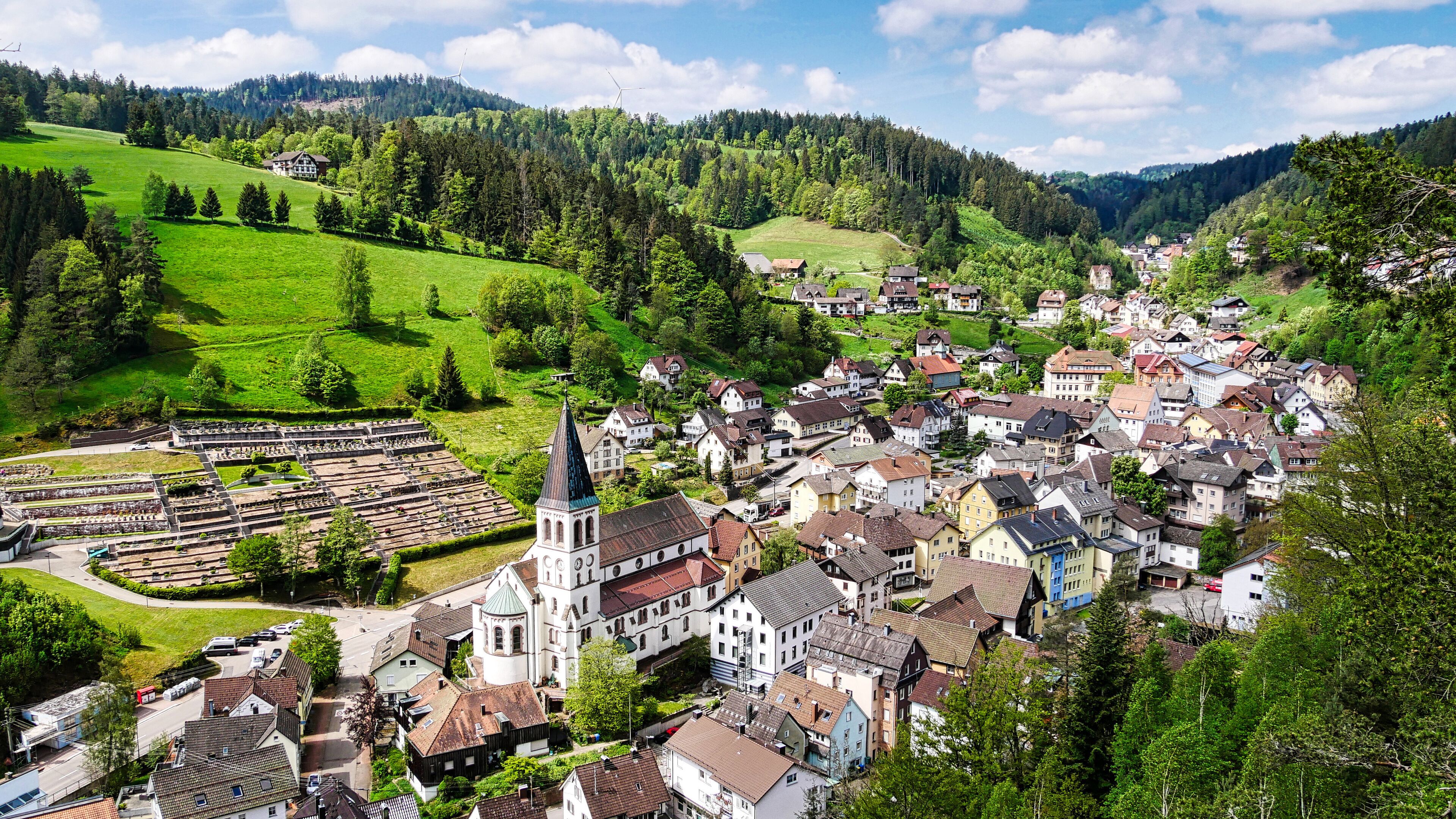 A picturesque village with a church, houses, and a wind turbine on a hill.
