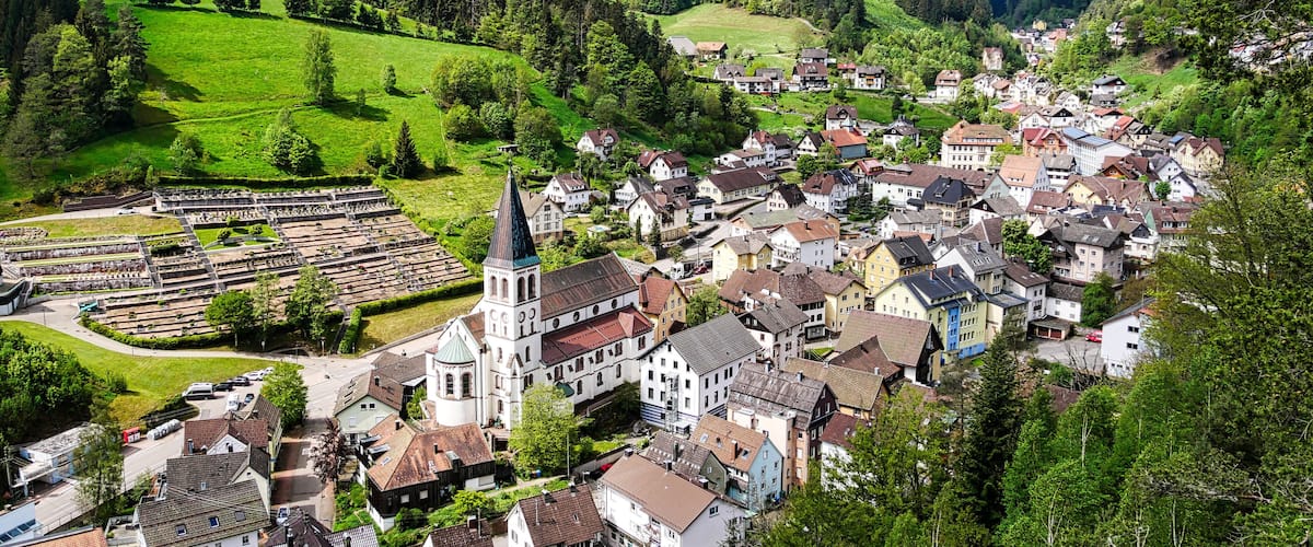 A picturesque village with a church, houses, and a wind turbine on a hill.