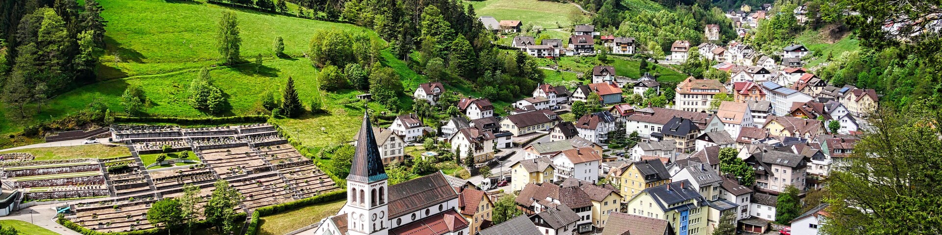 A picturesque village with a church, houses, and a wind turbine on a hill.