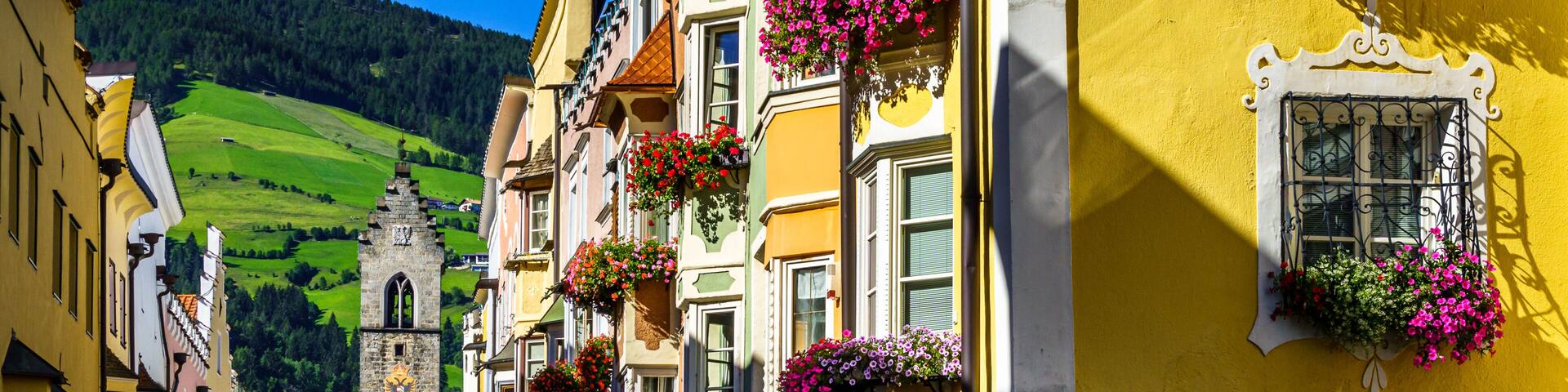 A colorful street with buildings adorned with flower boxes and a clock tower in the background.