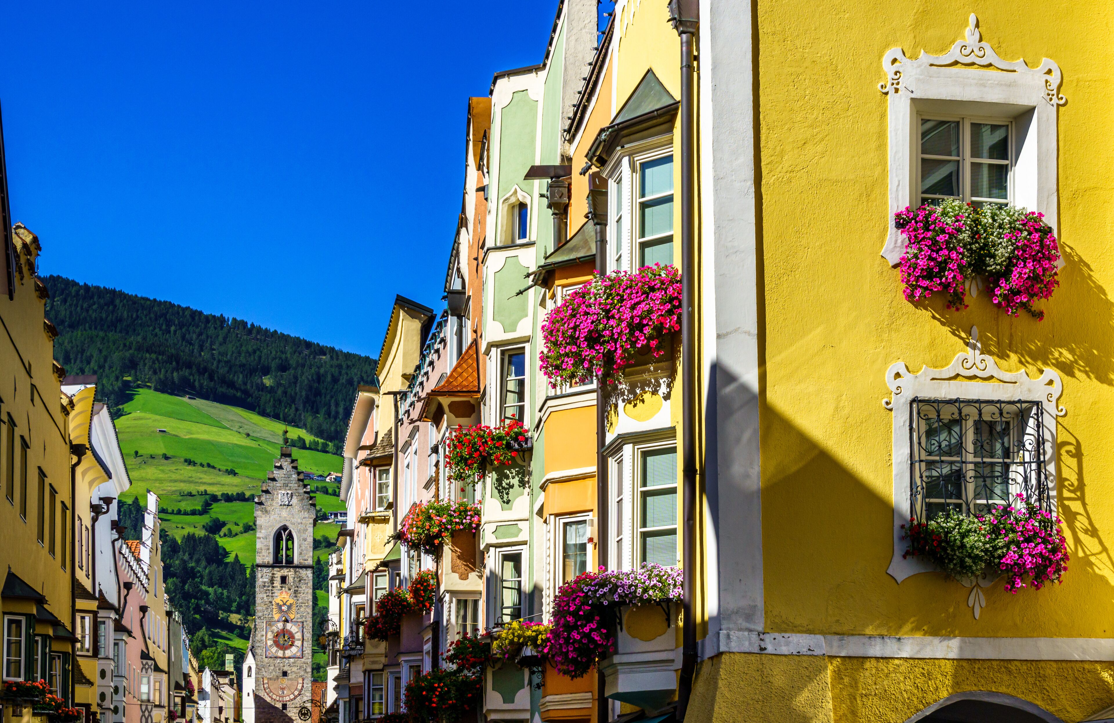 A colorful street with buildings adorned with flower boxes and a clock tower in the background.