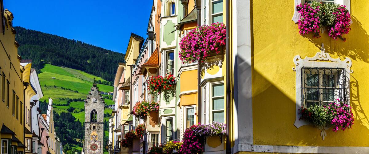 A colorful street with buildings adorned with flower boxes and a clock tower in the background.